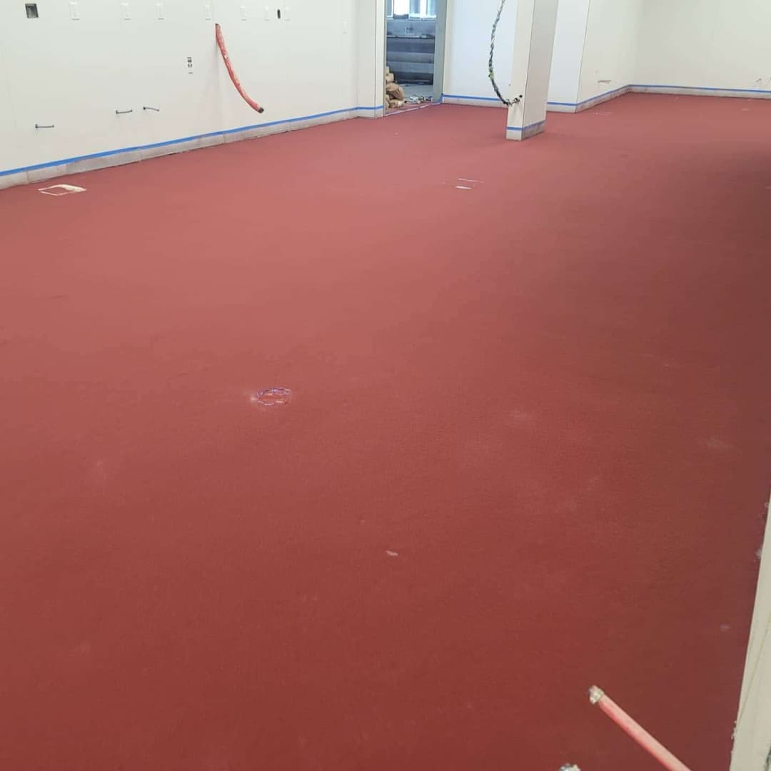 Red flooring in an empty room with unfinished walls and visible construction materials.