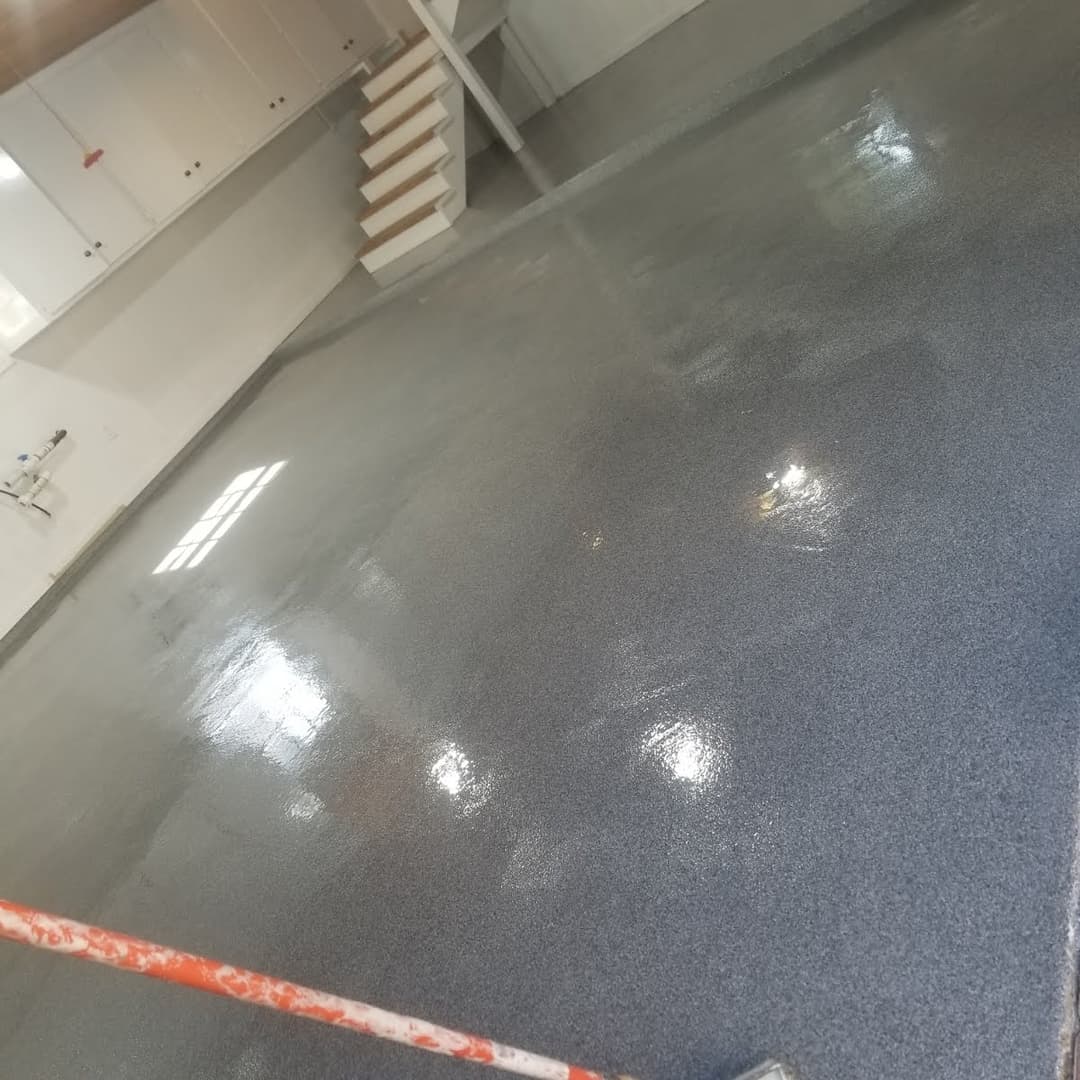 Shiny, newly coated gray epoxy floor in a spacious garage with stairs and cabinets.
