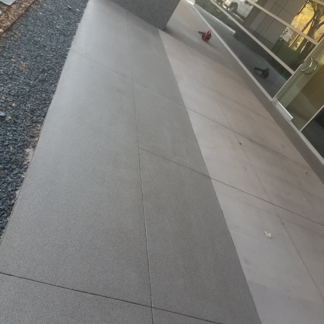 Gray concrete walkway with smooth surface, bordered by gravel, adjacent to a building.