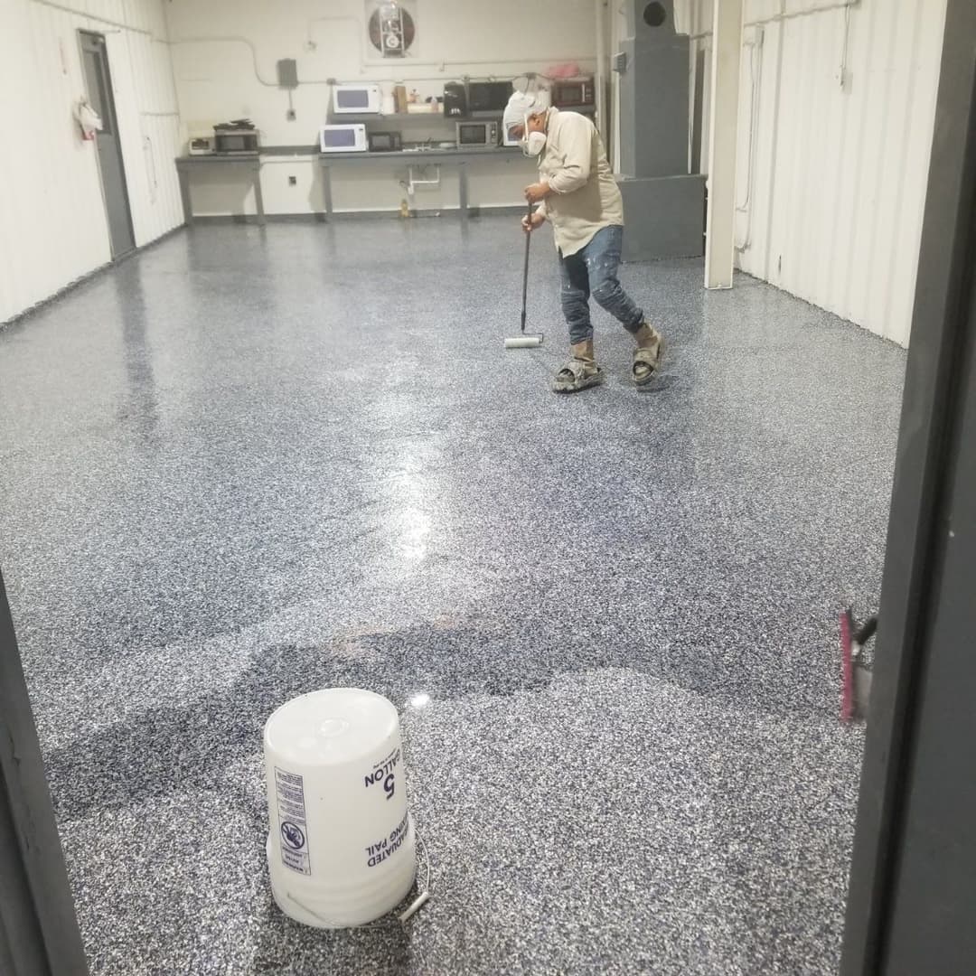 Person applying epoxy coating on a polished floor in a commercial kitchen space.