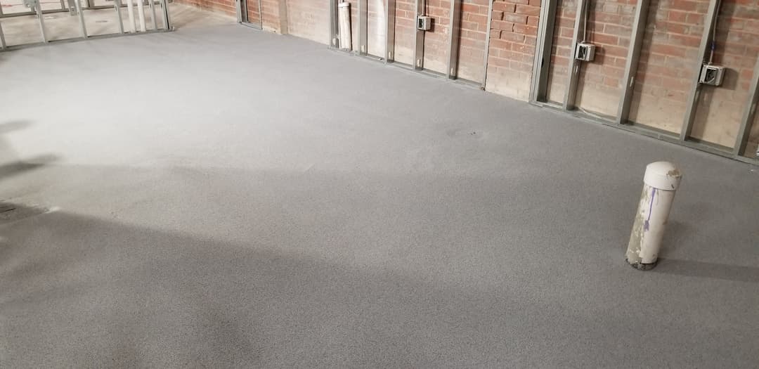 Newly installed gray flooring in an unfinished industrial interior space.