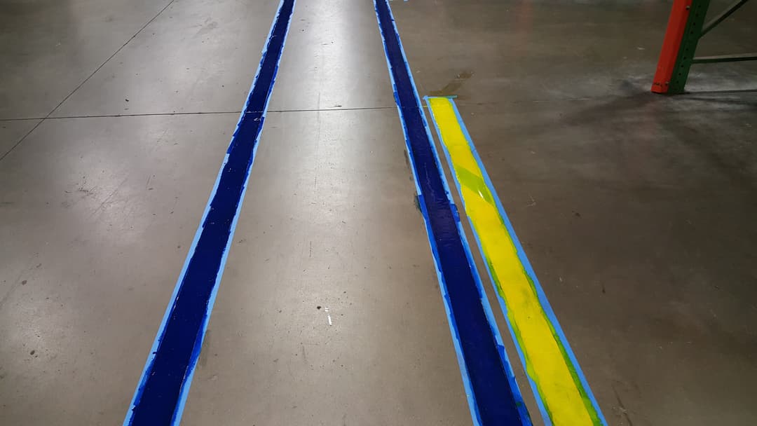 Blue and yellow safety lines painted on a warehouse floor for hazard demarcation.