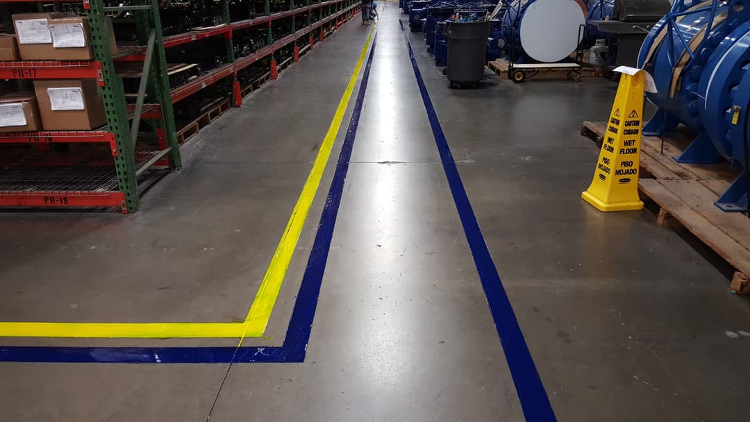 Warehouse floor marked with yellow and blue safety lines, wet floor caution sign visible.
