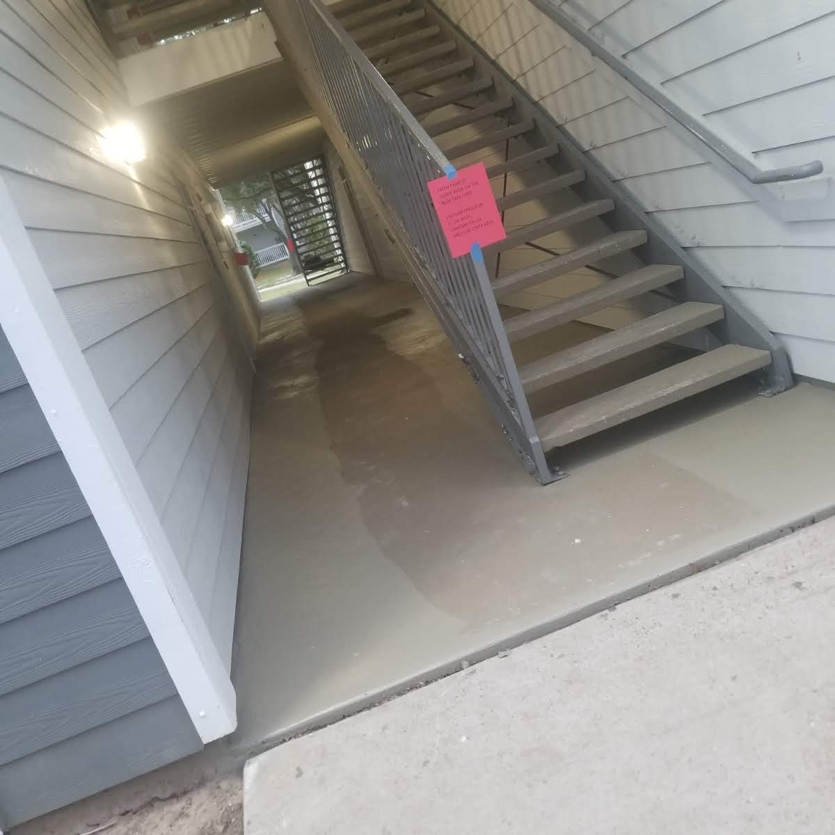 Newly poured concrete floor in apartment building hallway with staircase and wet sign.