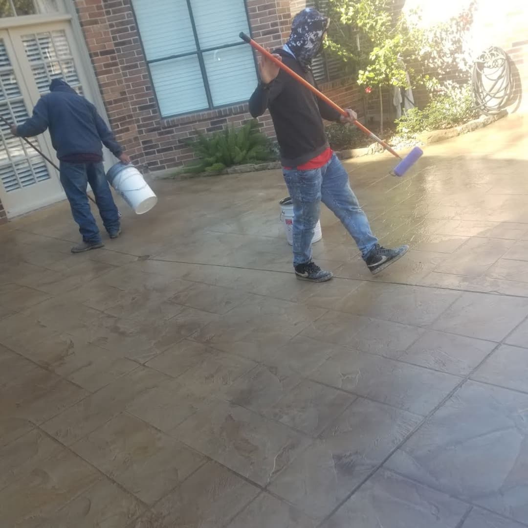 Workers applying a protective coat on a stamped concrete patio with rollers and buckets.