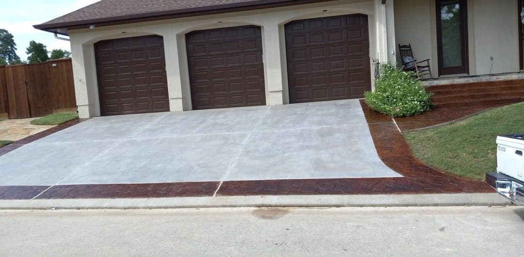 Decorative stamped concrete driveway and garage with brown doors and landscaping elements.