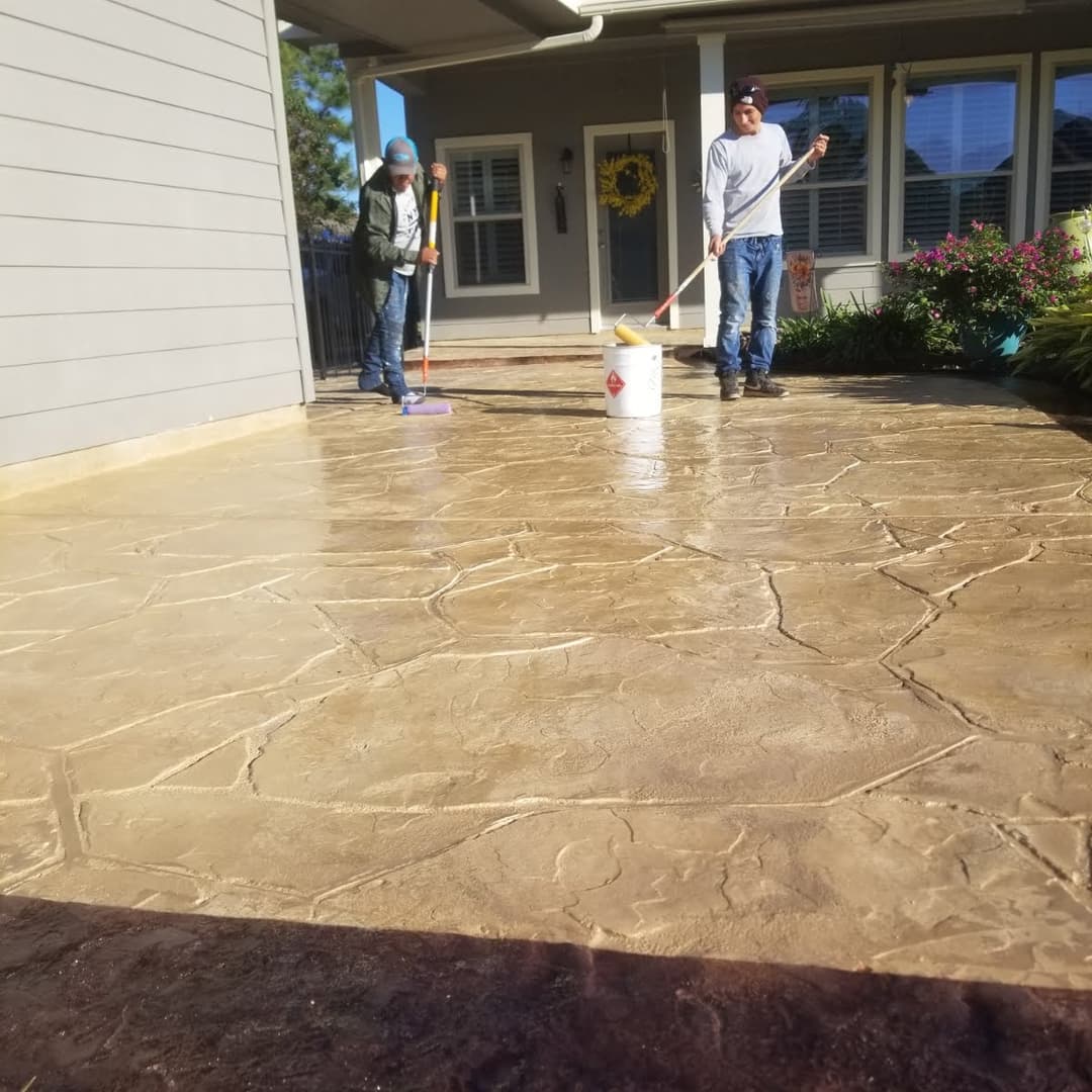 Two workers applying decorative stain on a stamped concrete patio at a residential home.