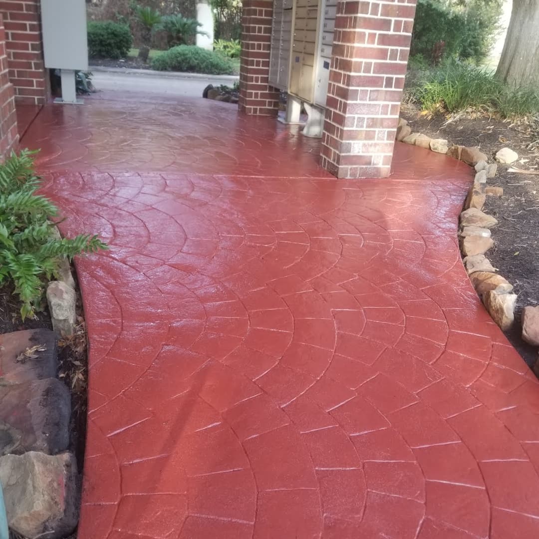 Decorative stamped concrete pathway with a rich red finish, bordered by natural stone landscaping.