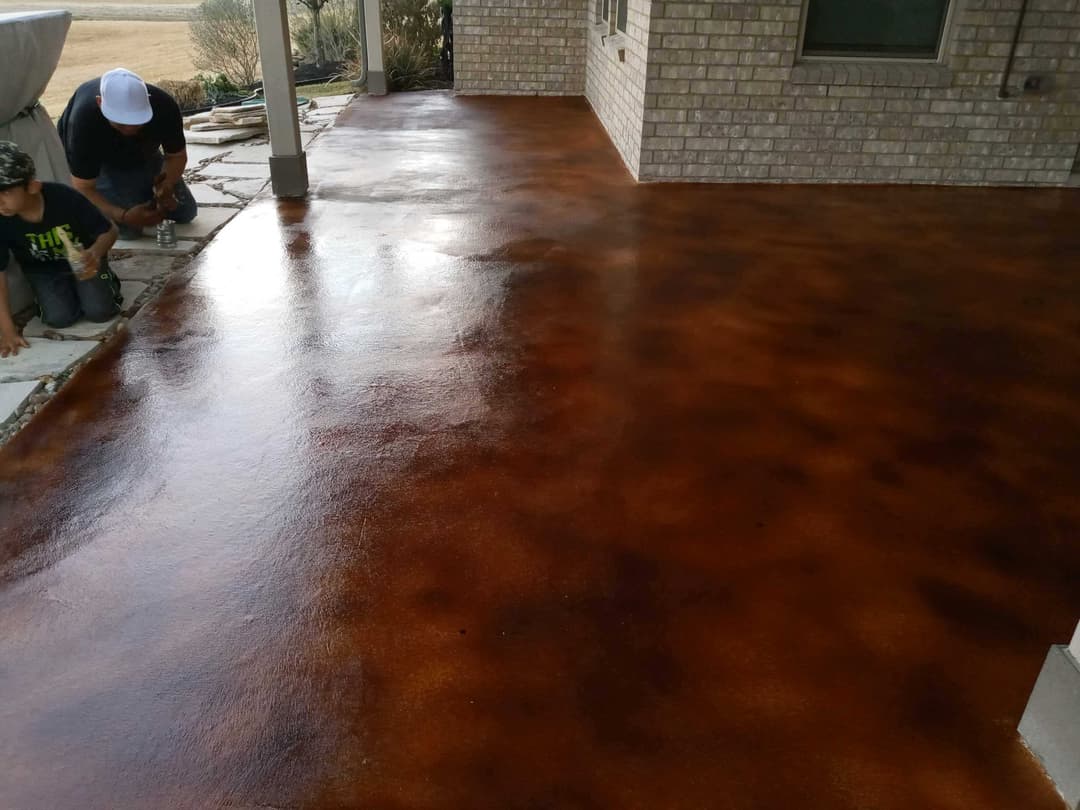 Workers applying a decorative stained finish to a concrete patio surface.