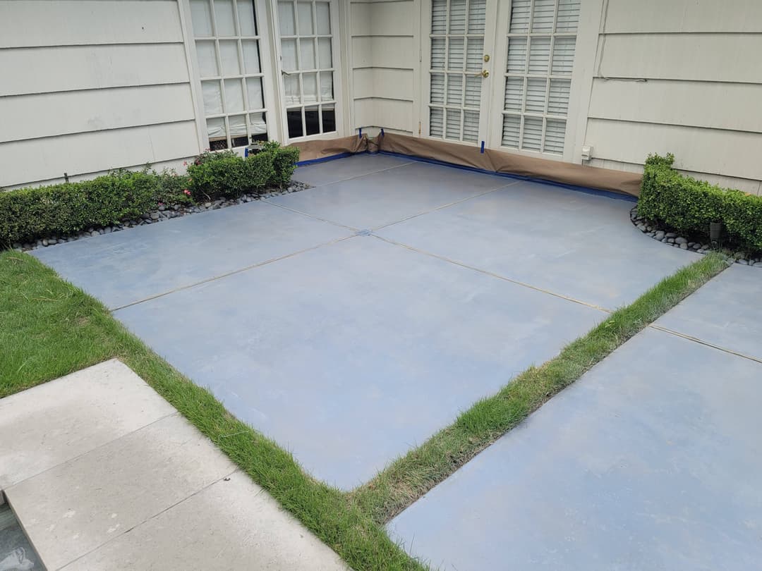 Freshly poured and leveled concrete patio with manicured shrubs and grass border.