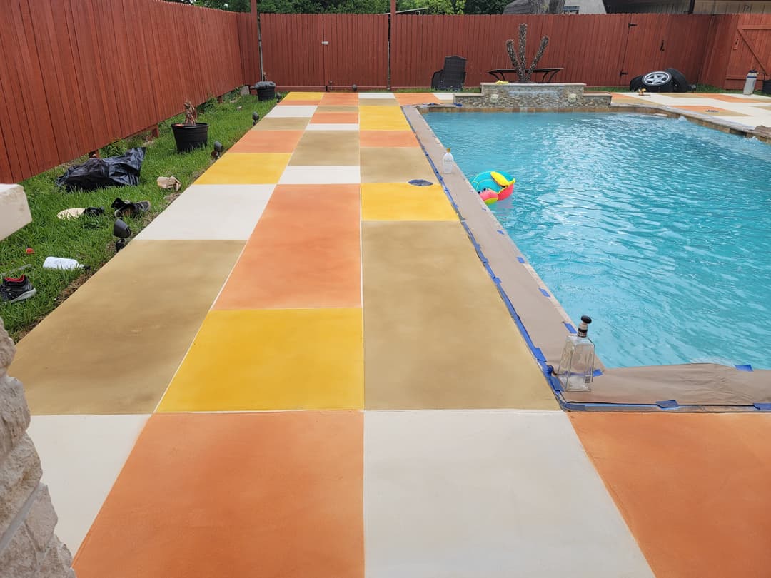 Decorative concrete patio in vibrant colors beside a swimming pool with landscaping elements.