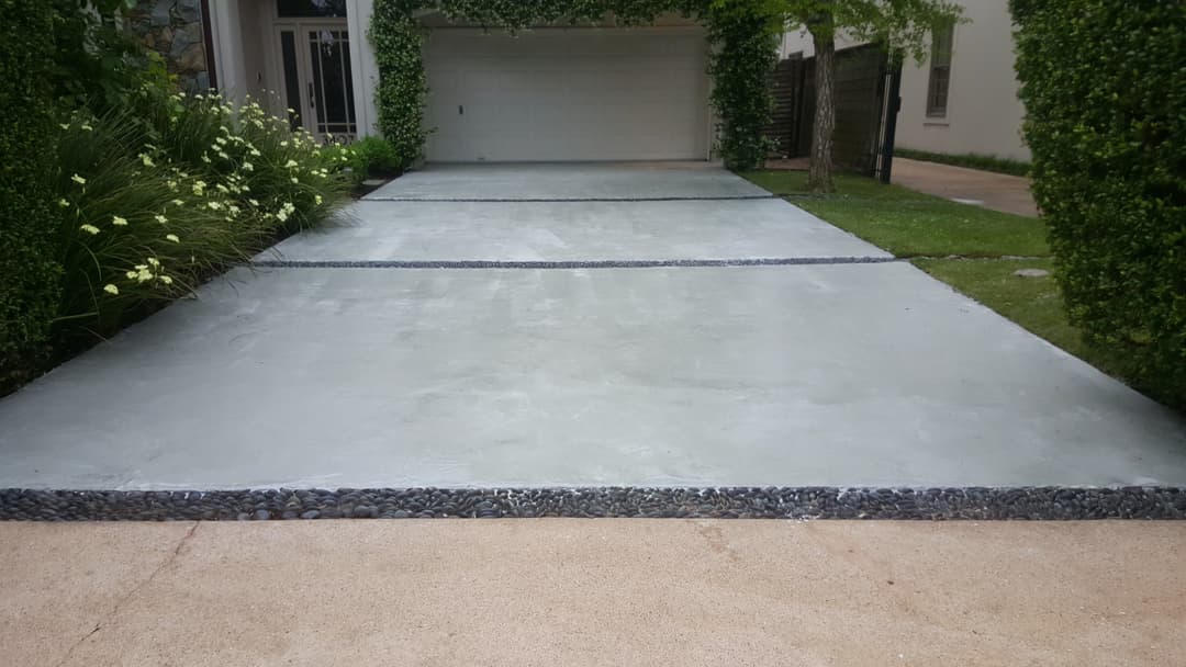 Modern concrete driveway with stone edges, lush greenery, and a garage in the background.