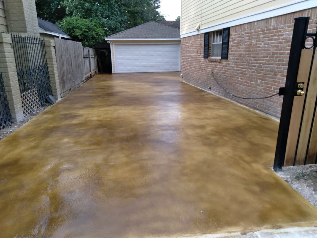Freshly finished concrete driveway with brown stain, adjacent to a brick home and garage.