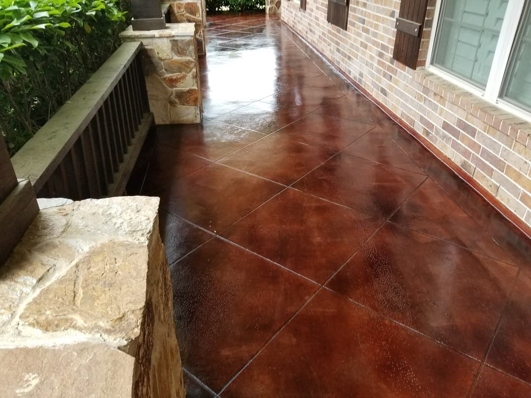 Stained concrete patio with a glossy finish and natural stone accents, surrounded by greenery.