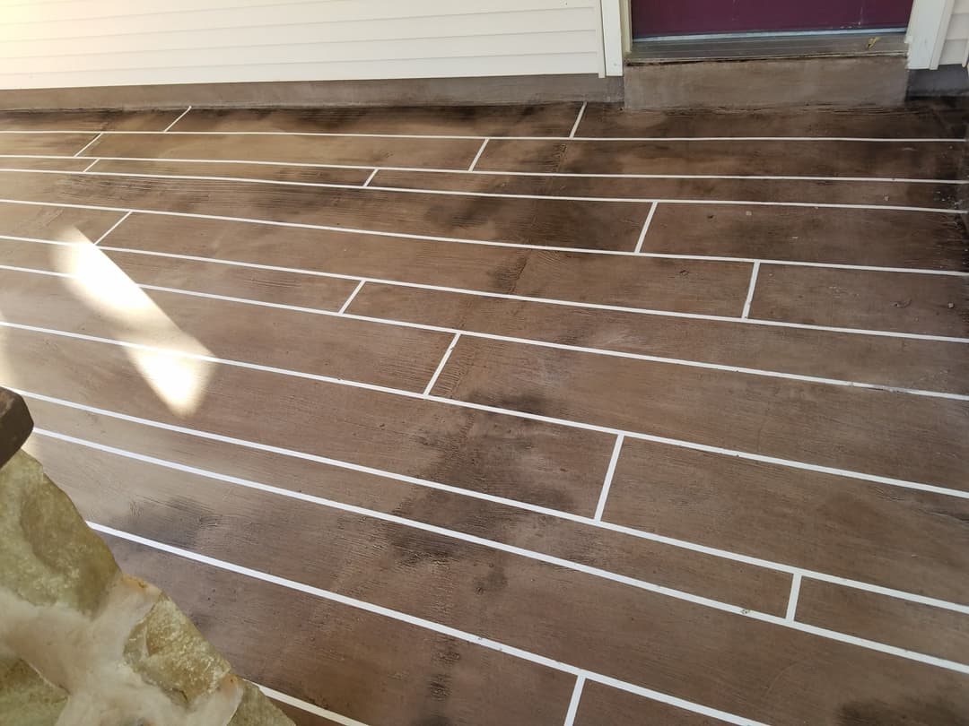 Clean, textured brown patio surface with white grout lines and sunlight highlighting the detail.