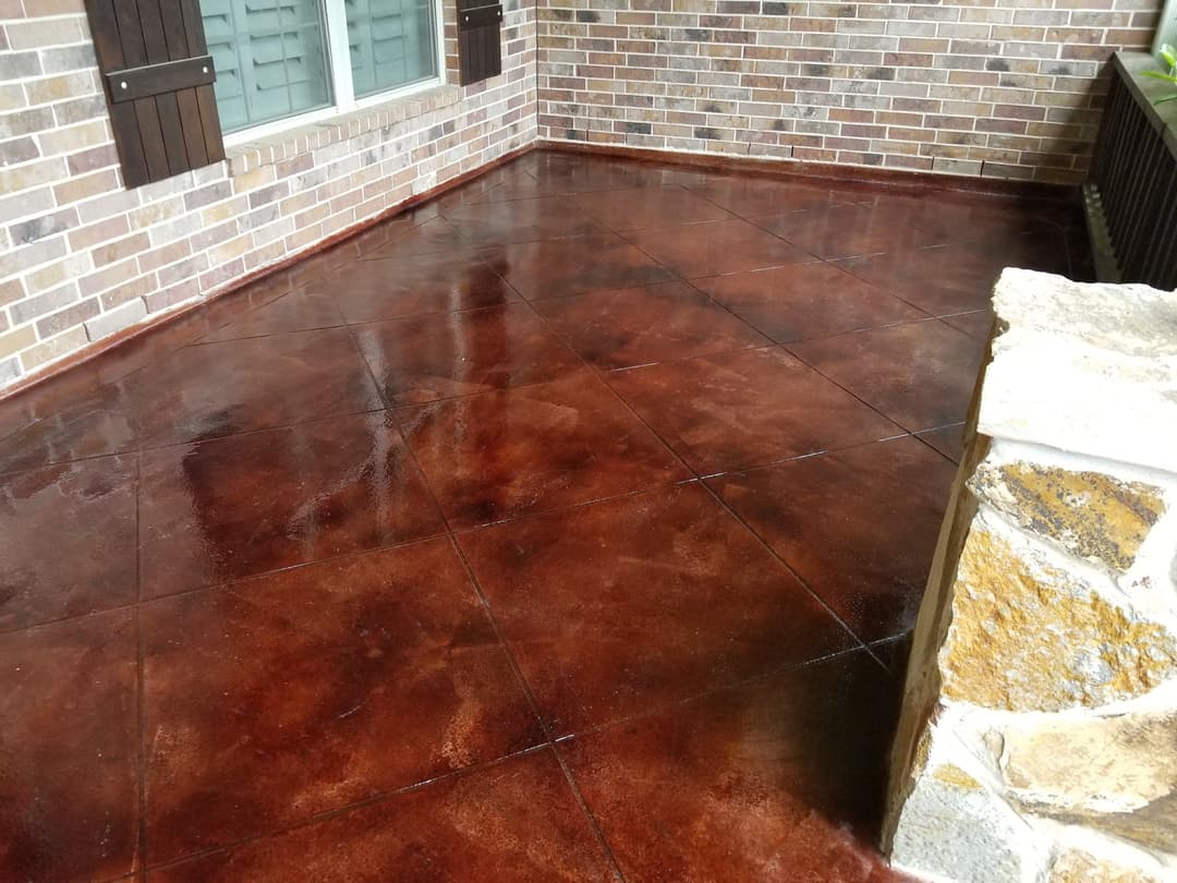 Stained concrete patio with a glossy finish and stone accents, showcasing rich brown tones.