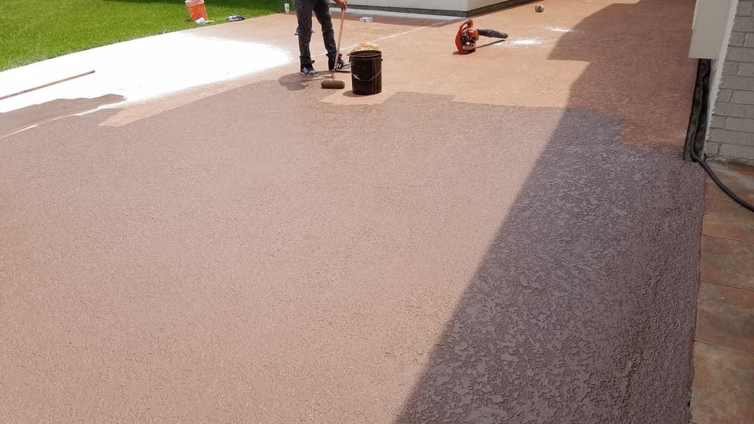 Worker applying sealant to a newly finished concrete patio with tools nearby.