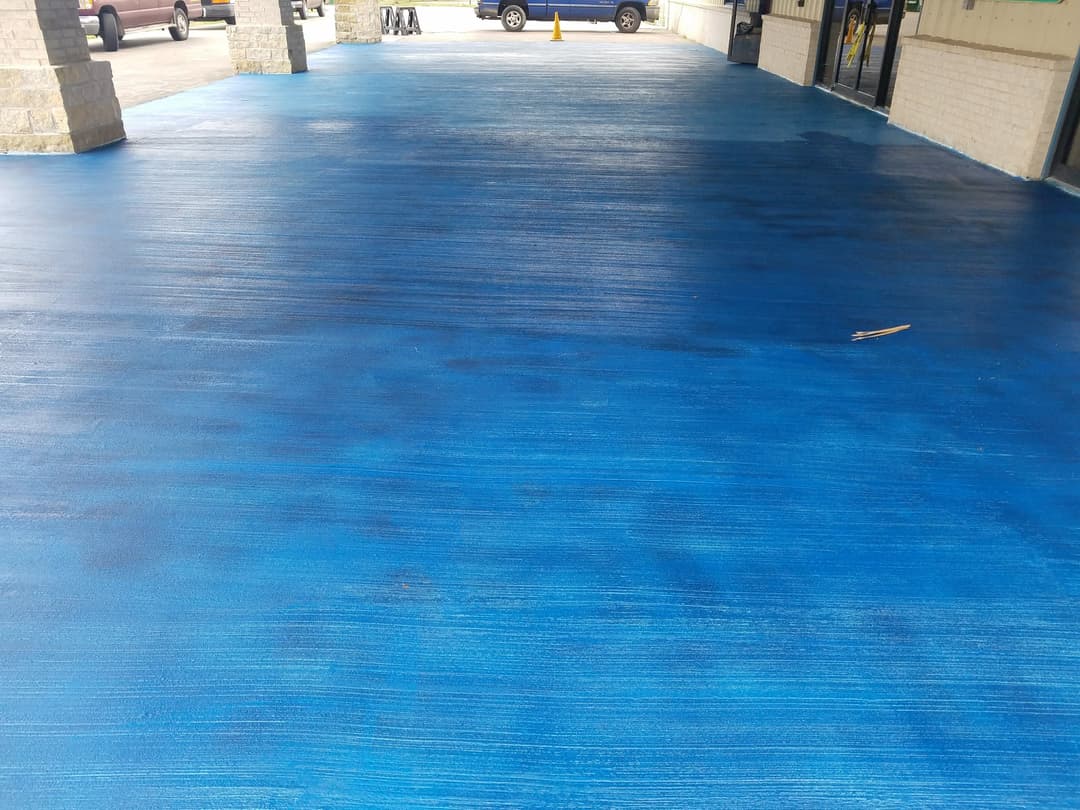 Blue painted floor under a covered walkway, with vehicles parked nearby.