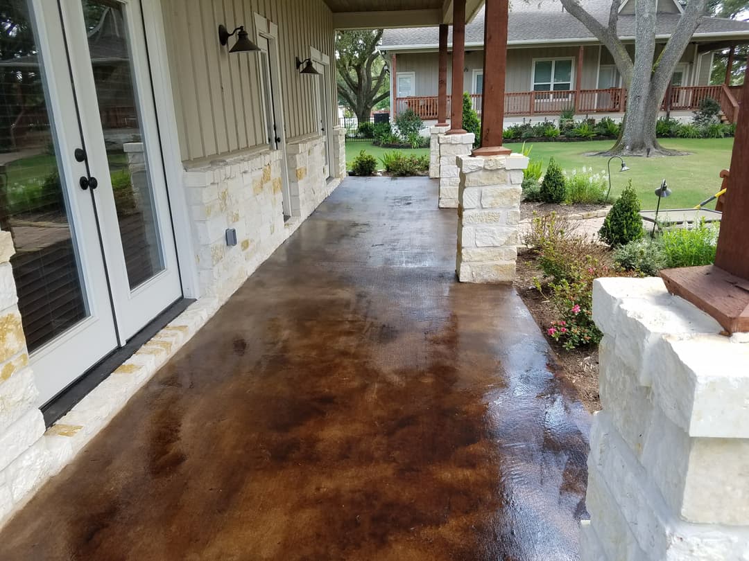 Beautiful stained concrete porch with stone columns and garden landscaping. Perfect outdoor space.