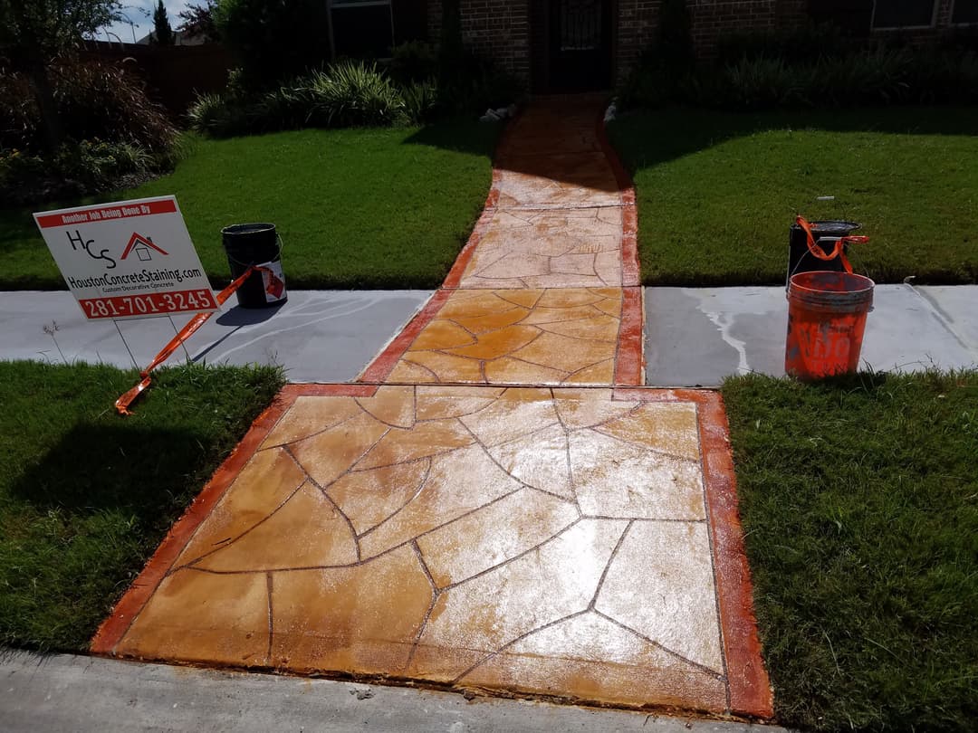 Decorative concrete walkway with brown and orange finish, tools and sign for landscaping service.