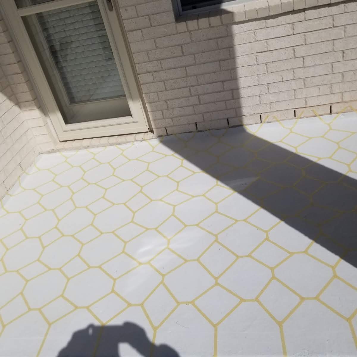 Freshly painted patio floor with a white base and yellow hexagonal pattern, sunlight casting a shadow.