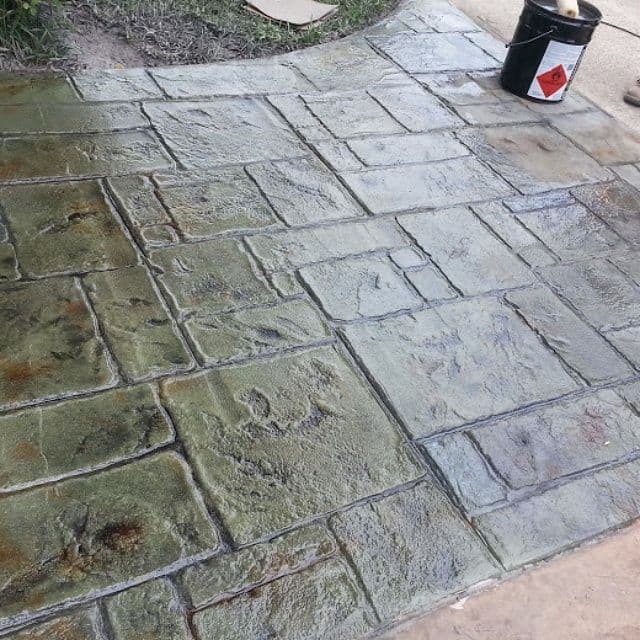 Textured stamped concrete surface in earthy tones with a paint bucket nearby.