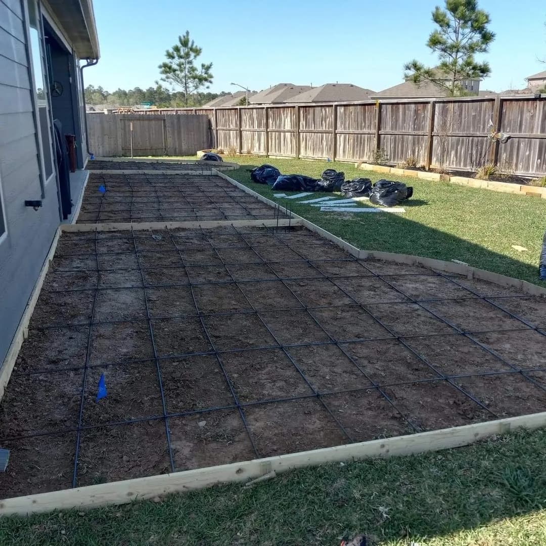 Concrete slab foundation preparation in a residential backyard with rebar grid and wooden forms.