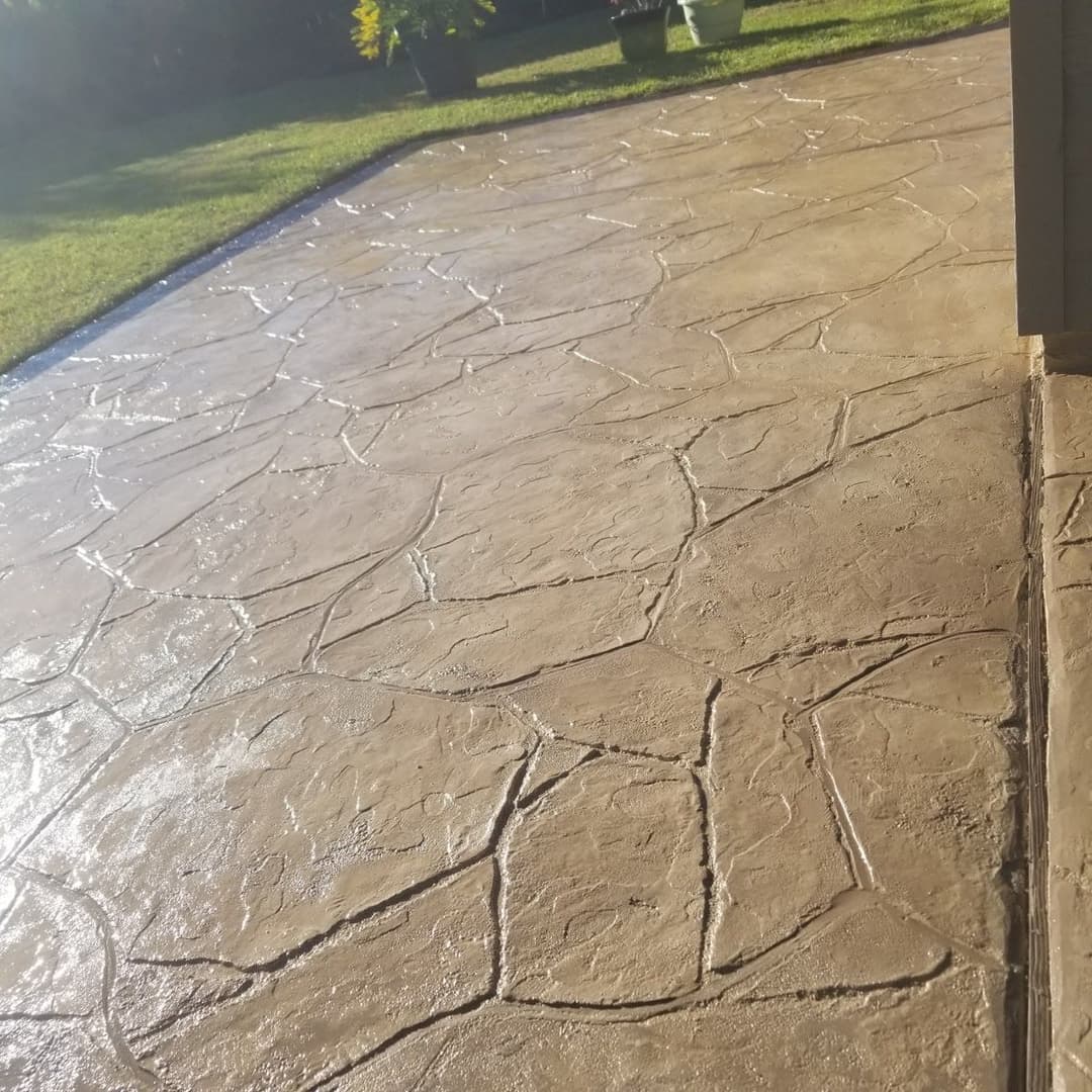 Decorative stamped concrete patio with textured stone pattern and green garden backdrop.