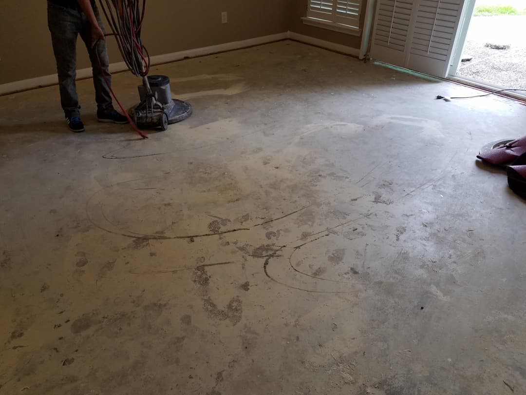 Person using a floor grinder on a dusty concrete surface in an empty room.