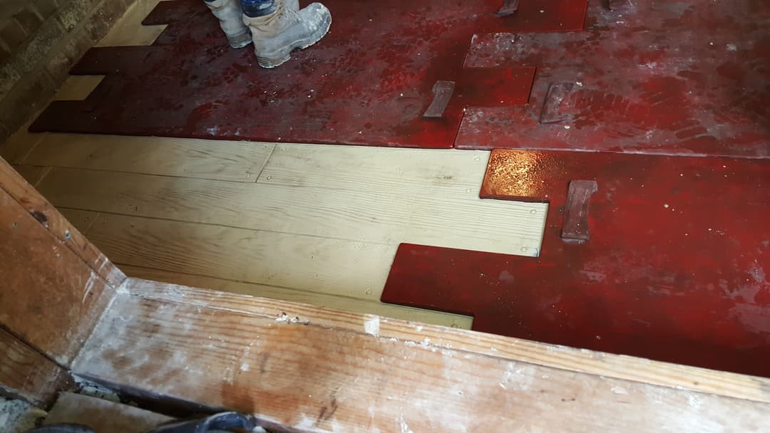 Person installing hardwood flooring next to red underlayment, showcasing construction progress.