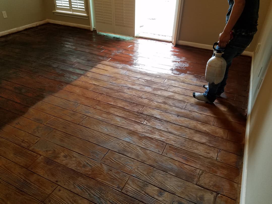 Person applying stain to hardwood floor in entryway, showcasing different wood tones.