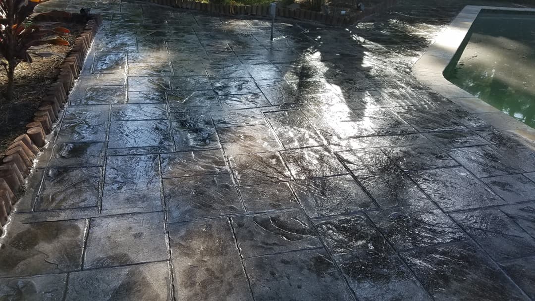 Stamped concrete patio with glossy finish and reflections, near a swimming pool.