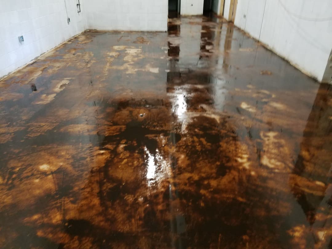 Stained concrete floor in a dimly lit room, showing significant wear and discoloration.