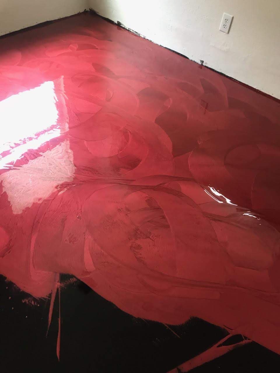 Red abstract art covering a glossy floor surface with black accents in a bright room.
