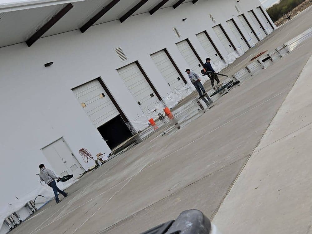 Workers cleaning a warehouse loading area with water and equipment.