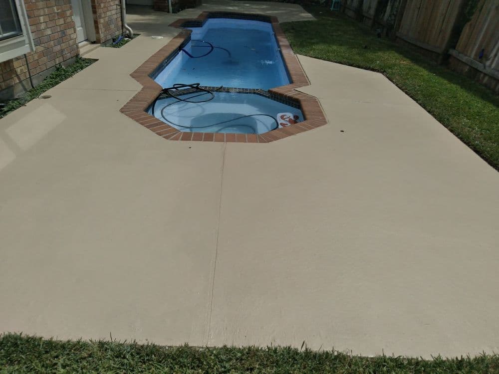 Swimming pool with brown tiled edge, surrounded by a clean concrete deck and green lawn.