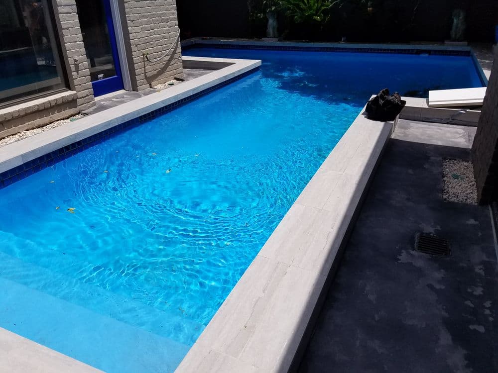 Modern swimming pool with clear blue water and stone deck, surrounded by greenery.