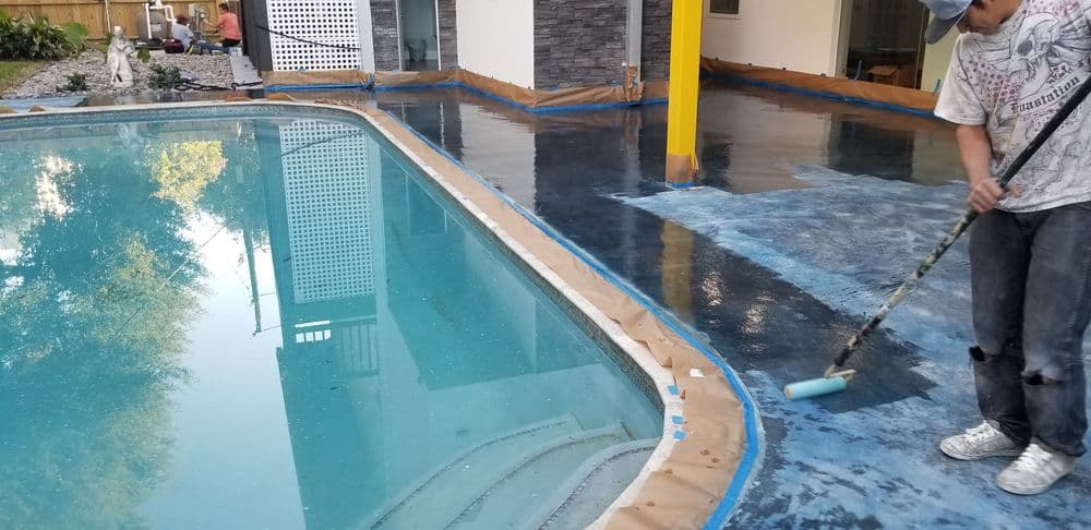 Person applying sealant by a poolside, with protective measures in place.